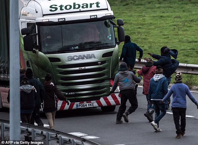 A Sudanese migrant has died after trying to jump onto the roof of a moving Britain-bound lorry from the top of a Calais road toll booth (stock image of migrants trying to block a truck on one of the access roads for the Eurotunnel in 2015