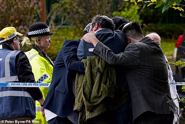Members of the Jewish community comfort each other near Heaton Park Synagogue in Manchester following a terror attack last year