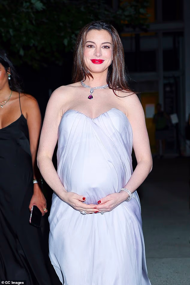Pregnant Anne Hathaway showed off her baby bump in a chic mauve gown at the Bvlgari exhibition in New York on Wednesday night