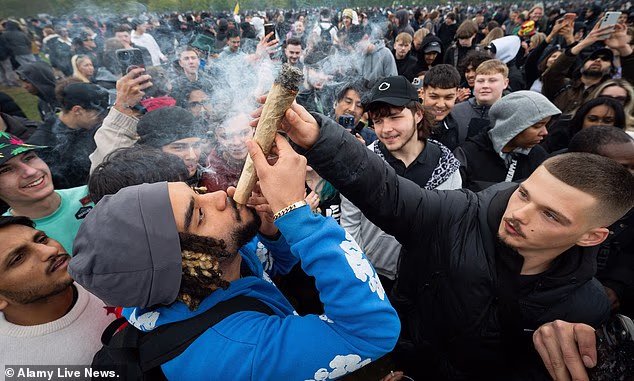 A man smokes from an oversized spliff at a pro-cannabis rally in Hyde Park, London, while surrounded by onlookers