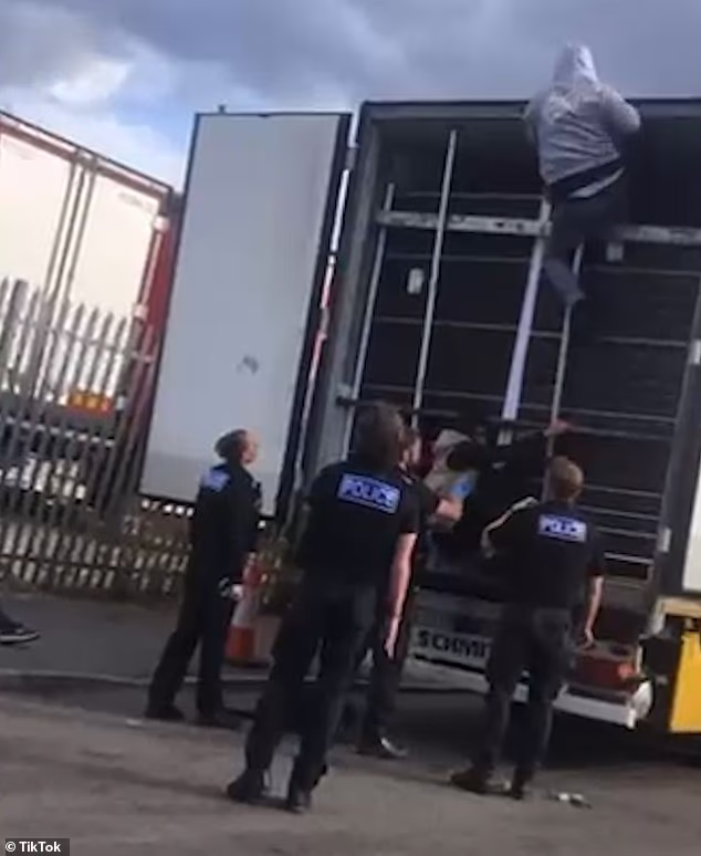 Men, believed to be migrants and wearing hooded tracksuits, can be seen clambering down from a height within the lorry as officers wait for them to reach the ground