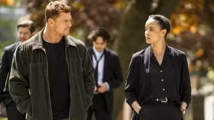Alan Ritchson as Jack Reacher walking with Maria Sten as Frances Neagley at her father's funeral in Neagley