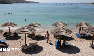 The beach with the sea in the background. There are sun beds and straw shades
