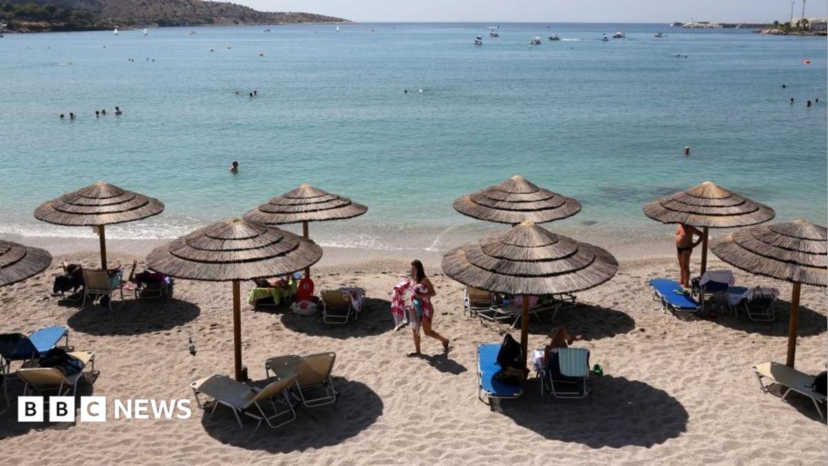 The beach with the sea in the background. There are sun beds and straw shades