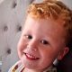Three-year-old Noah Woods, with light hair and wearing a brightly coloured top, smiles at the camera.