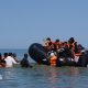 People thought to be migrants attempt to board a small boat off the coast of Hardelot, France, during an attempt to cross the English Channel on 29 July 2026. A group of people are on the inflatable vessel wearing orange life jackets and others are in the water, waiting to board the dinghy.