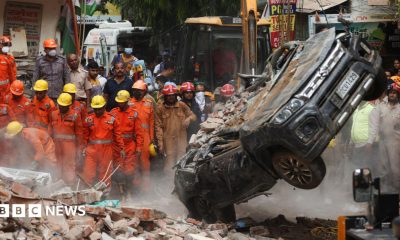 National Disaster Response Force (NDRF) personnel look on at a building collapse in Delhi, while a crushed car is pulled by a digger from the rubble.