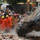 National Disaster Response Force (NDRF) personnel look on at a building collapse in Delhi, while a crushed car is pulled by a digger from the rubble.