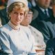 Princess Diana, wearing a light blue dress and hat, sits in between a young Prince William on the left (holding his hand to his mouth) and Harry to the right. Diana is looking into the distance to the left.