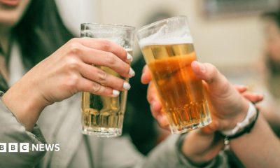 A pair of beer-filled glasses being knocked together in a bar setting.