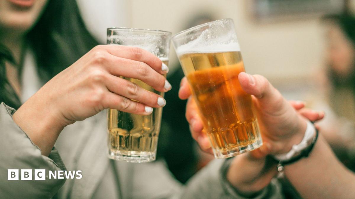 A pair of beer-filled glasses being knocked together in a bar setting.