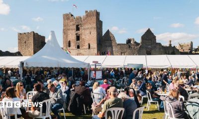 Crowds of people, some of them seated, with marquees in the distance and a castle behind them