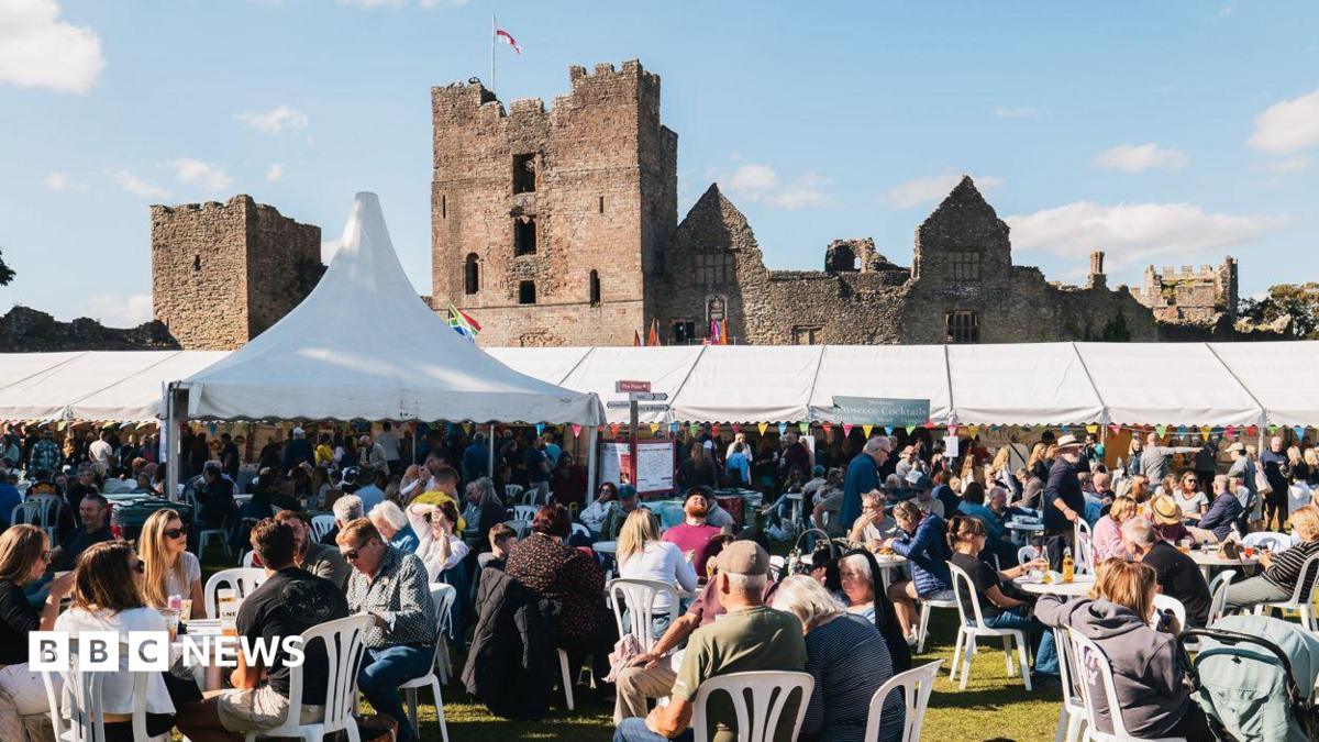 Crowds of people, some of them seated, with marquees in the distance and a castle behind them