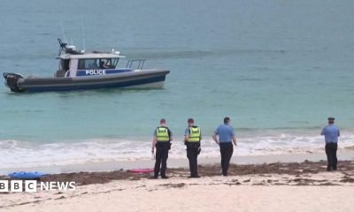 Police officers stand on Sorrento Beach while a police boat patrols offshore during search and recovery operations after a fatal shark attack