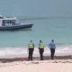 Police officers stand on Sorrento Beach while a police boat patrols offshore during search and recovery operations after a fatal shark attack