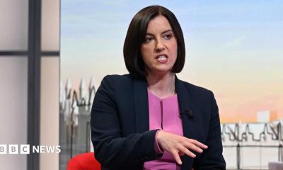 Bridget wears a navy blazer over a purple top sitting and talking in front of the illustrated Sunday with Laura Kuenssberg set.