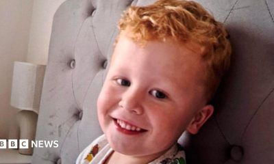 Three-year-old Noah Woods, with light hair and wearing a brightly coloured top, smiles at the camera.