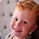 Three-year-old Noah Woods, with light hair and wearing a brightly coloured top, smiles at the camera.