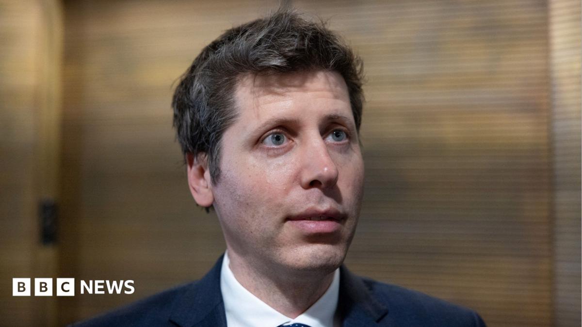 OpenAI CEO Sam Altman standing before a lobby of elevators answering questions from reporters.