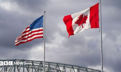 An American and Canadian flag flutter on poles over a bridge.