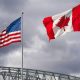 An American and Canadian flag flutter on poles over a bridge.