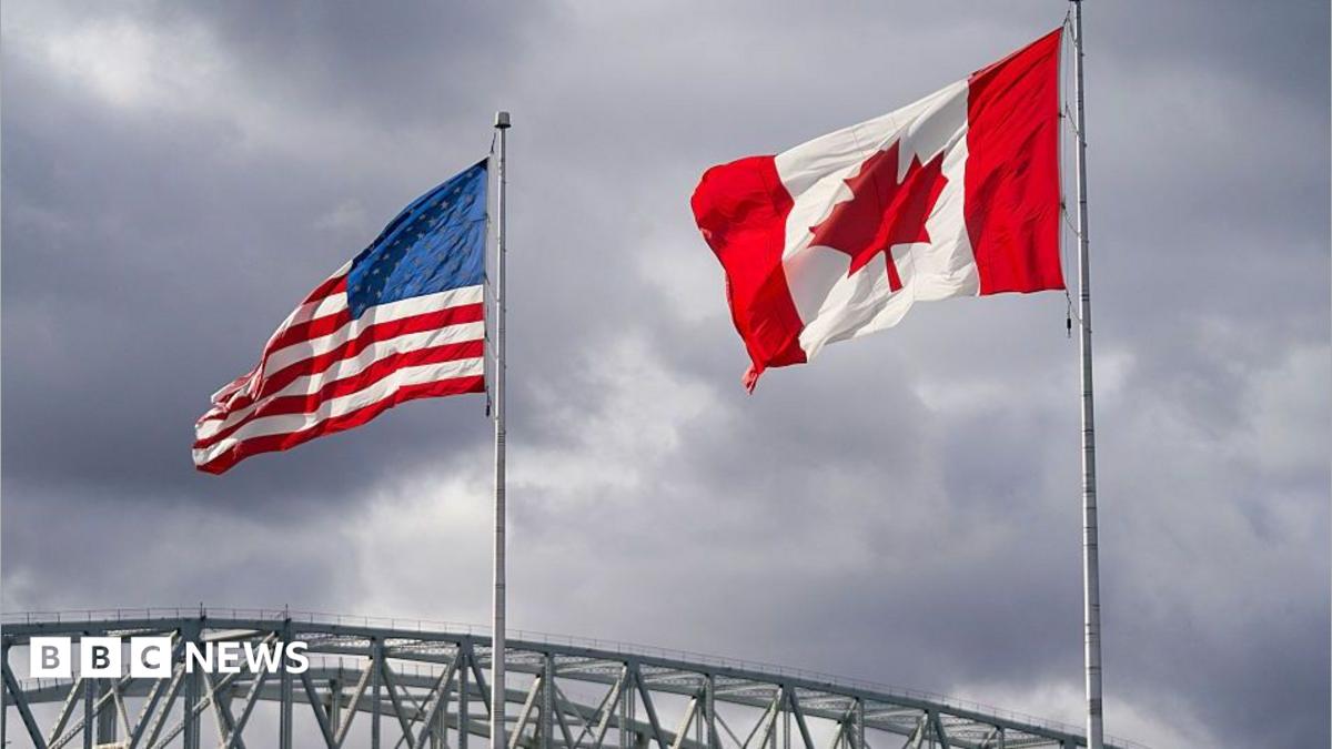 An American and Canadian flag flutter on poles over a bridge.