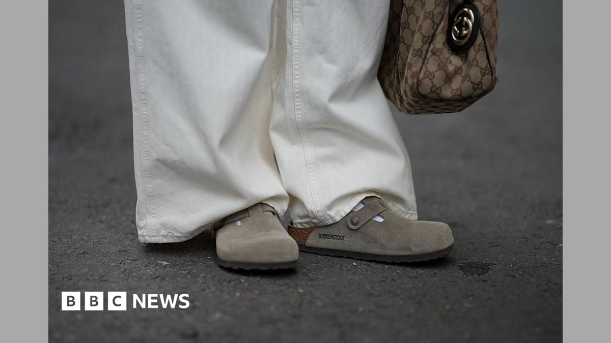 A person is seen wearing cream-white wide-leg jeans with subtle stripes and Boston clogs in soft suede with an open back and adjustable strap from Birkenstock.
