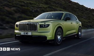 A green Bentley SUV is driven along a road with a hill behind it.