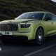 A green Bentley SUV is driven along a road with a hill behind it.