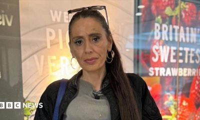 A woman with long, dark hair that is tied up in a ponytail. She is wearing a grey T-shirt and black jacket. She is looking into the camera with a straight face. She is wearing large, gold hoop earring and has a pair of sunglasses on top of her head.