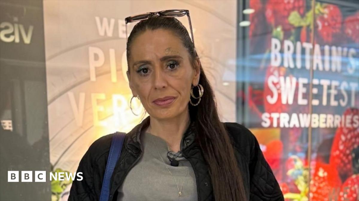 A woman with long, dark hair that is tied up in a ponytail. She is wearing a grey T-shirt and black jacket. She is looking into the camera with a straight face. She is wearing large, gold hoop earring and has a pair of sunglasses on top of her head.