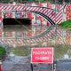 A flooded footpath leading to an underpath with warning cones and a "footpath closed" sign