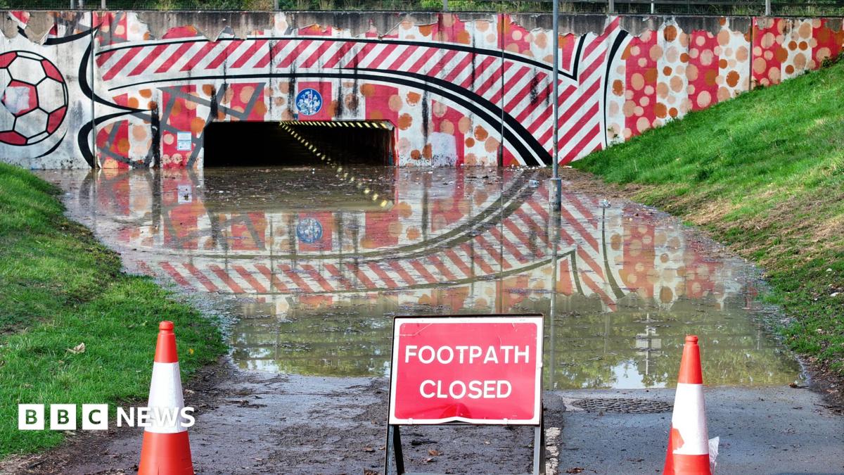 A flooded footpath leading to an underpath with warning cones and a "footpath closed" sign