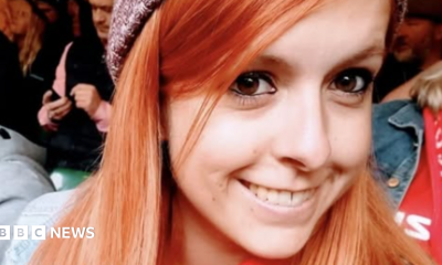 Danielle is shown smiling and wearing a beanie hat in a crowd. Her hair is ginger coloured and she is looking at the camera with her brown eyes.