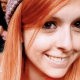 Danielle is shown smiling and wearing a beanie hat in a crowd. Her hair is ginger coloured and she is looking at the camera with her brown eyes.