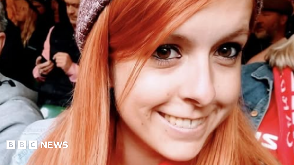 Danielle is shown smiling and wearing a beanie hat in a crowd. Her hair is ginger coloured and she is looking at the camera with her brown eyes.