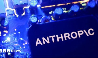 A smartphone display showing the Anthropic logo in black letters on an all-white background, laid on a laptop keyboard lit in pink and purple