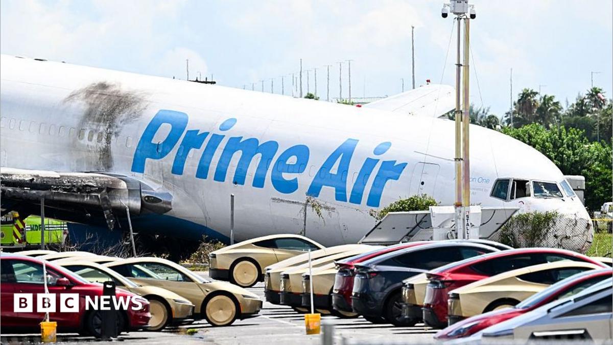 A parking lot filled with Tesla Cybercabs is seen in the foreground as the nose of a Prime Air cargo plane rests on the ground after the aircraft overran the runway and struck cars the previous day at Miami International Airport in Miami, Florida, on September 7, 2026.