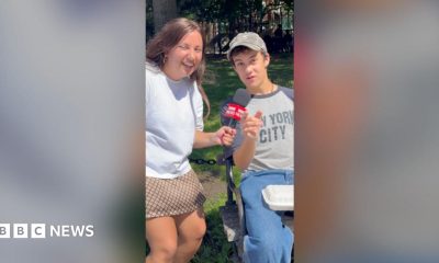Yasmin Rufo smiles while a young man points at the camera wearing jeans and a New York City T-shirt.