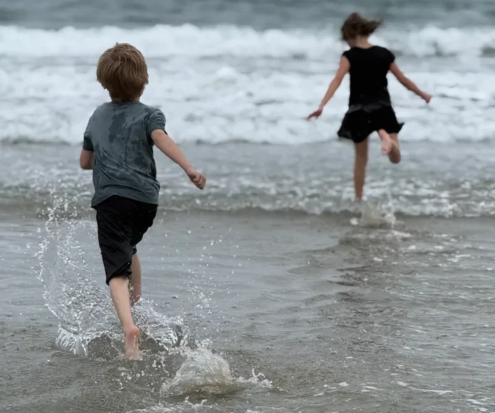 The author’s children run to the ocean while she photographs them.