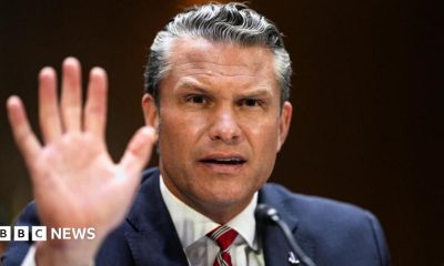 Pete Hegseth gestures by lifting his hand as he frowns