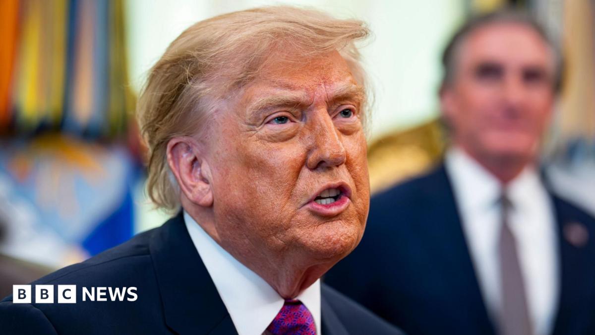 Donald Trump speaks, he is wearing a blue suit jacket, white shrit with a red and purple tie. The background is blurred.