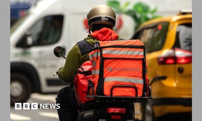 Person rides a moped with an brightly-coloured bag attached to the back with the logo reading Doordash