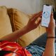 A picture of a woman in a red t shirt and jeans leaned back on a sofa checking her energy consumption on a mobile app.