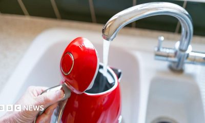 A person filling up a red kettle from the kitchen sink
