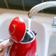 A person filling up a red kettle from the kitchen sink