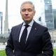 Champagne wears a suit and tie while he stands on a lawn in front of the Toronto city skyline of high-rise buildings.