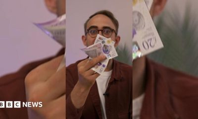 A man with glasses holds a bunch of bank notes in front of his face.