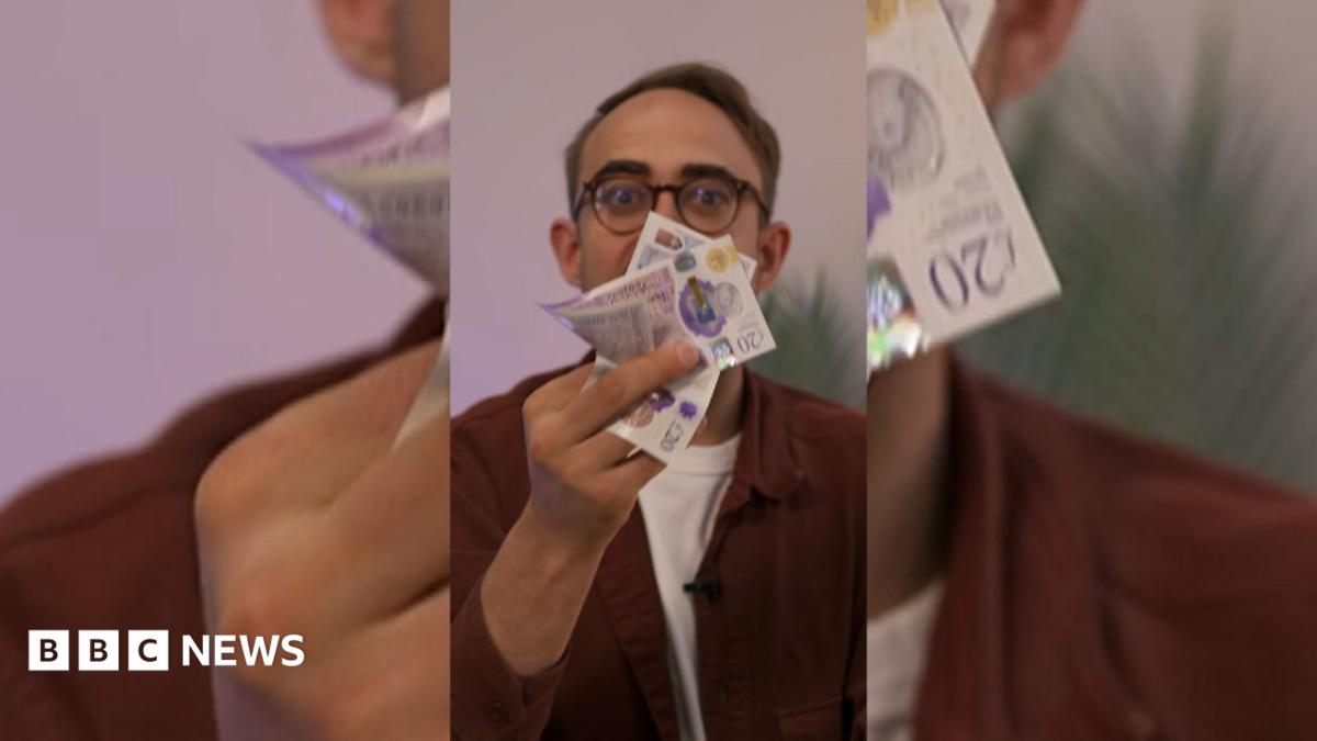 A man with glasses holds a bunch of bank notes in front of his face.