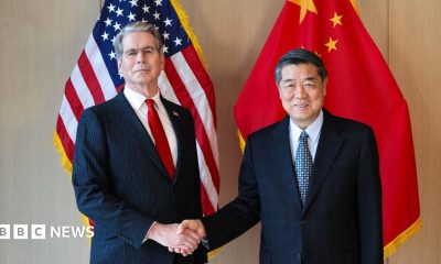 US Treasury Secretary Scott Bessent shakes the hand of China's top trade negotiator He Lifeng stand in front of both countries' flags.